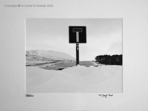 A road sign next to a road blocked by snow in the Derbyshire Peak District near Buxton